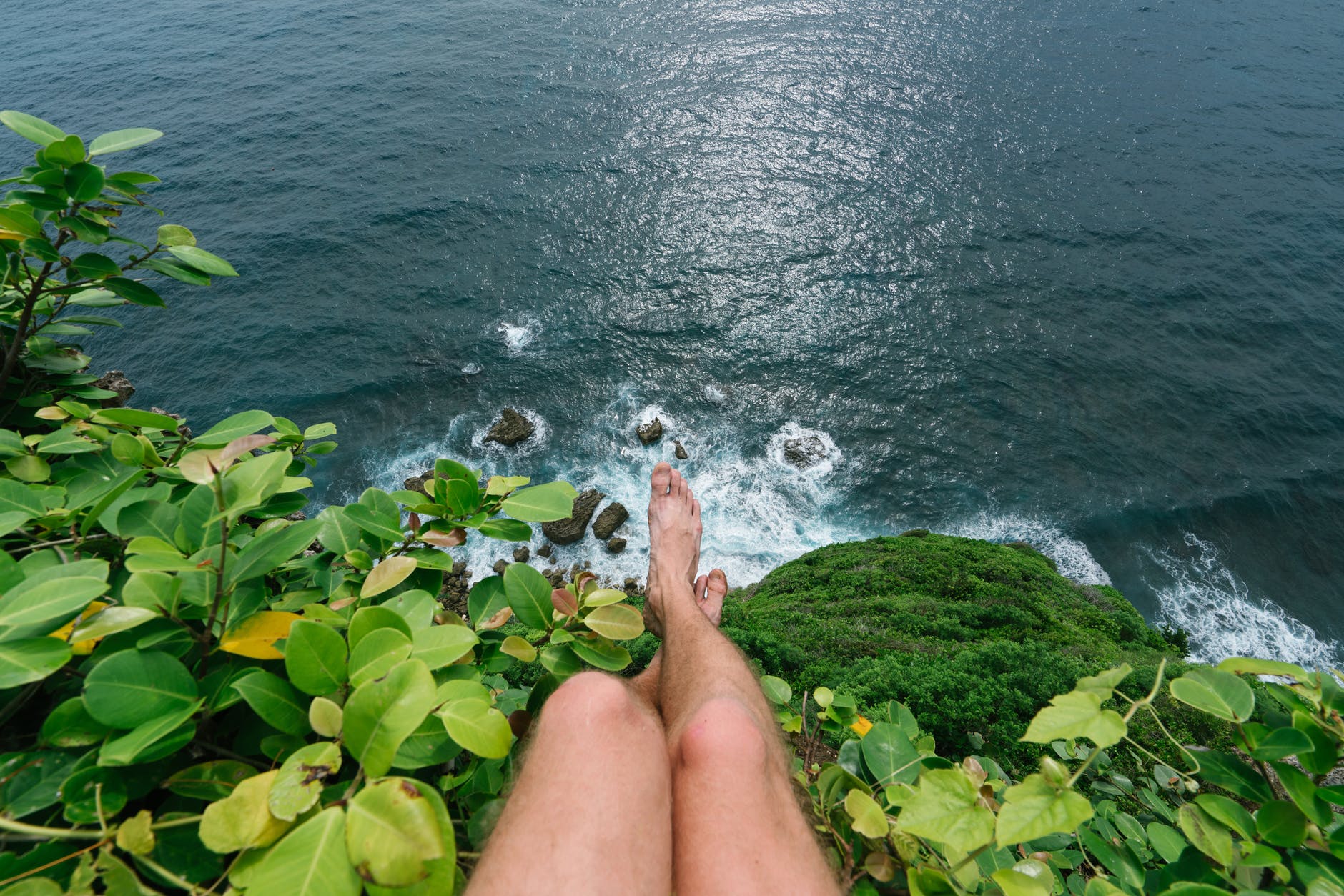 faceless barefoot man sitting on high cliff